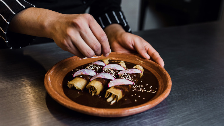 A person garnishing chicken mole enchiladas