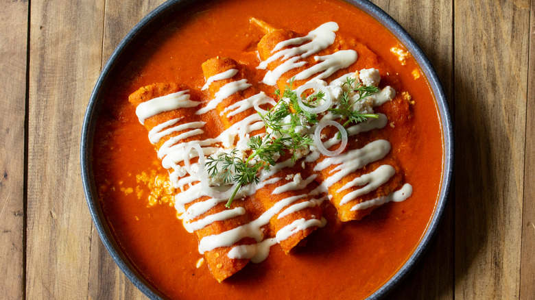 A plate of enchiladas rojas with crema, onions, and cilantro garnish