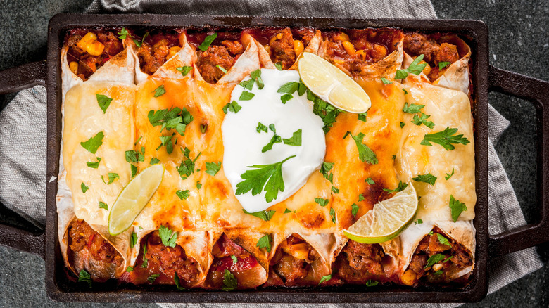 A pan of enchiladas garnished with sour cream, cilanto, and lime wedges
