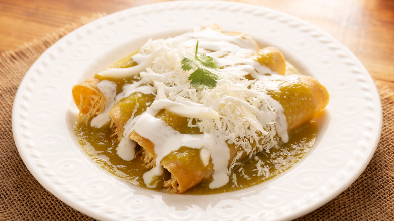 A plate of enchiladas verdes with chicken, crema, and queso