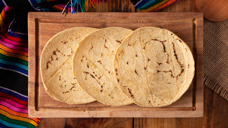 Three corn tortillas on a wooden cutting board