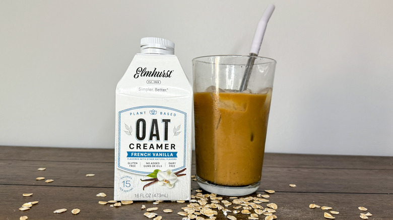 Carton of Elmhurst oatmilk creamer next to glass of iced coffee