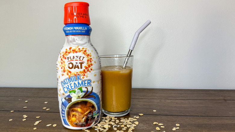 Container of Planet Oat Oatmilk Creamer next to a glass of iced coffee