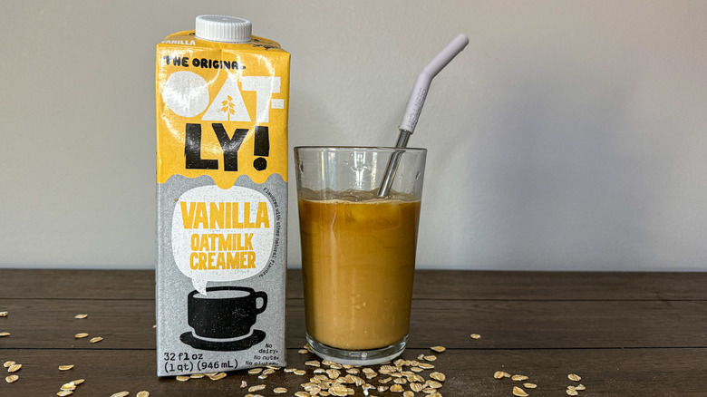 Carton of Oatly Vanilla Oat Milk Creamer next to glass of iced coffee