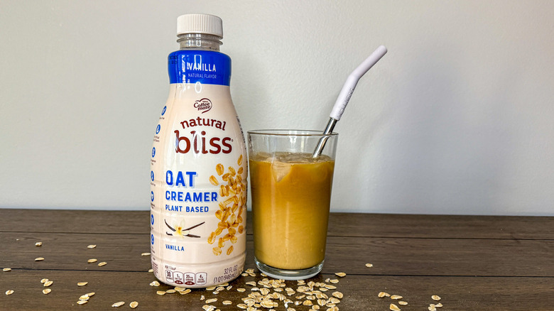 Container of Coffeemate natural bliss oat milk creamer next to glass of iced coffee