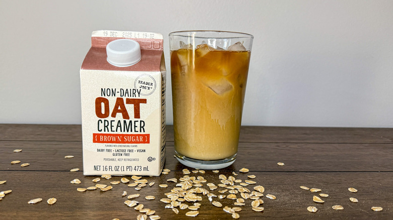 Carton of Trader Joe's non-dairy brown sugar oat creamer next to glass of iced coffee