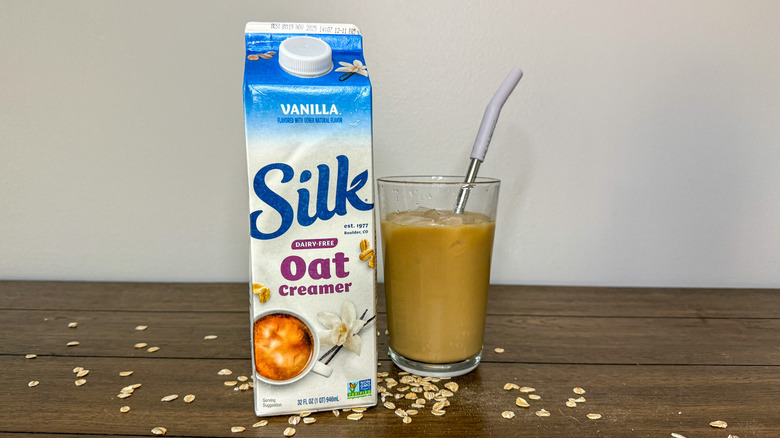 Carton of Silk Oat Vanilla creamer next to a glass of iced coffee