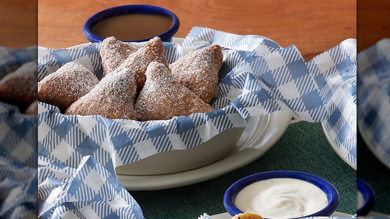 An order of biscuit beignets in a basket with dipping sauces