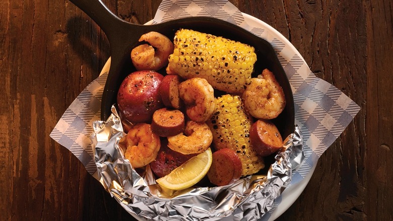 A skillet with shrimp, sausage, and corn