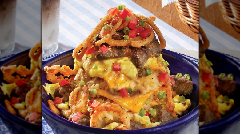 A blue bowl with hashbrown casserole with steak, eggs, and toppings