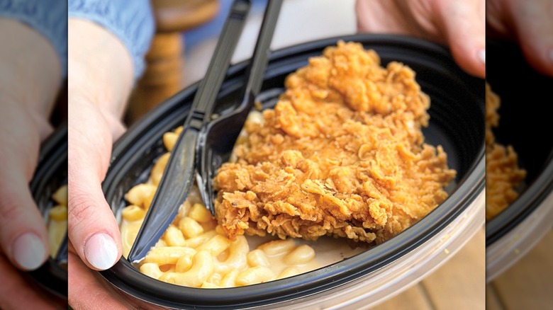 A to-go container with fried chicken and mac and cheese