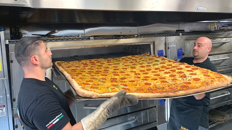 Employees taking giant pizza out of oven