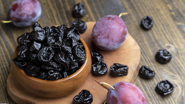 Bowl of prunes and whole plums on table