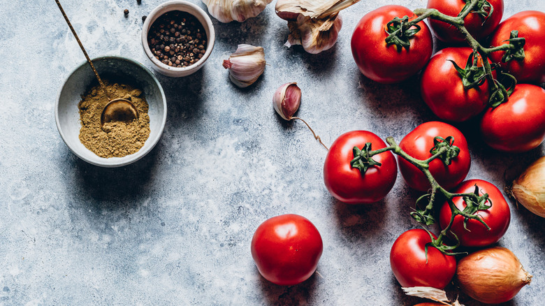 Tomatoes, onions, spices, and bell peppers on countertop