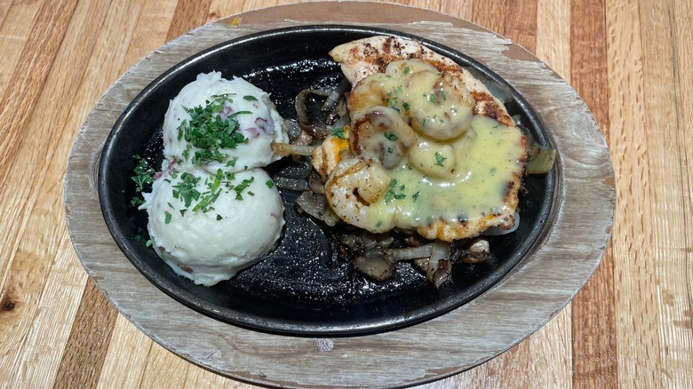 Two scoops of mashed potatoes and a chicken breast with shrimp and butter sauce sit in a skillet on a table.