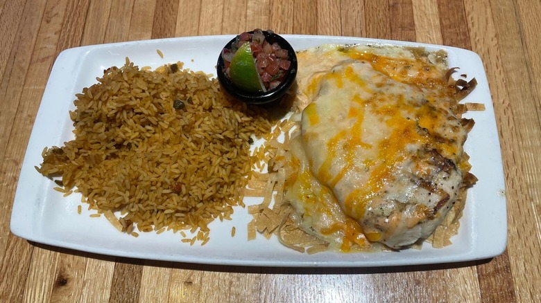 A cheesy chicken breast on a bed of tortilla strips sits on a plate with Mexican rice.