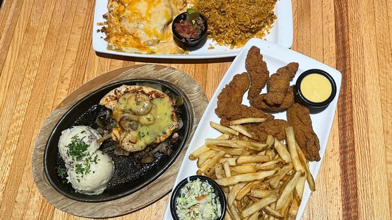 Fiesta Lime chicken plate, Bourbon Street Chicken and Shrimp plate, and Chicken Tenders platter all sit on a wood table.
