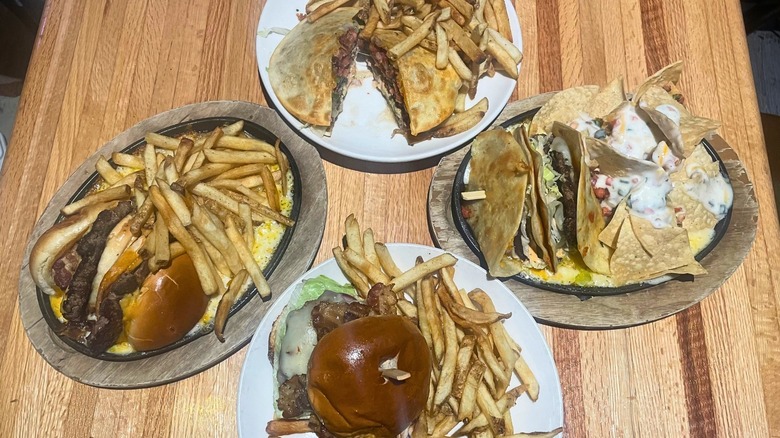 Four variations of burger dishes with fries sit on a wood table.