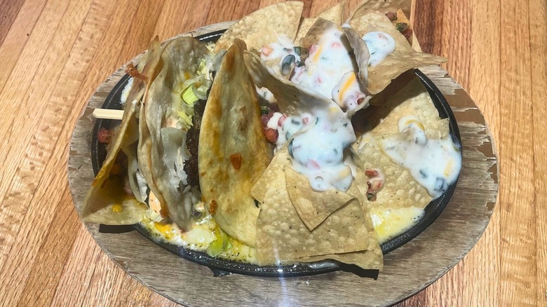 A burger in a quesadilla wrapper sits in a skillet of cheese with tortilla chips.