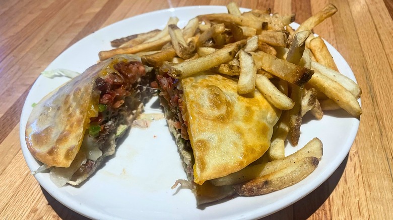 A Quesadilla Burger cut in half sits on a plate with fries.