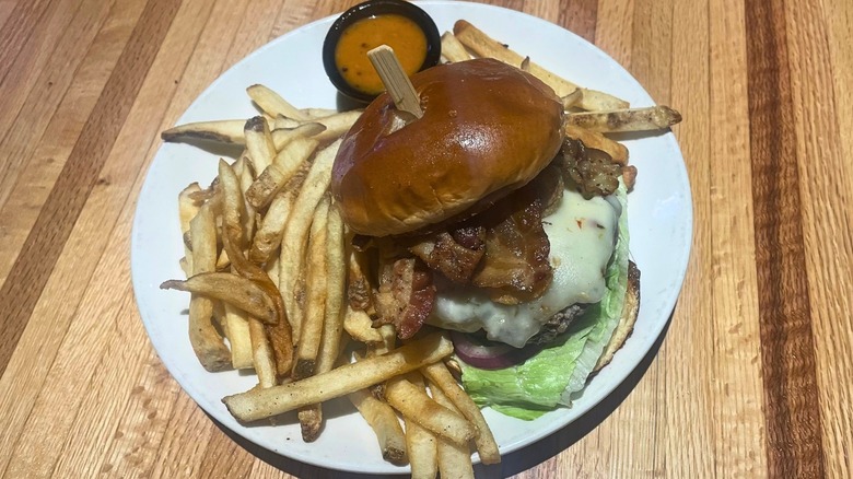 A loaded cheeseburger sits on a plate with whiskey sauce and fries.