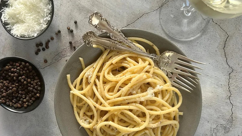 A large bowl of Bucatini Cacio E Pepe with two forks and fresh grated cheese on top