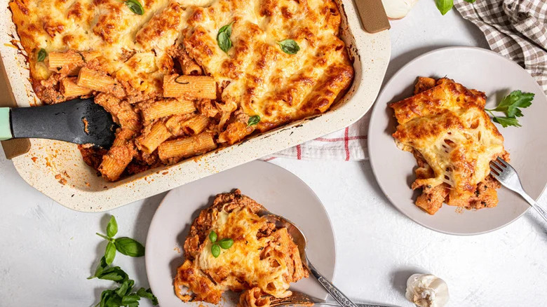 Casserole dish of Cheesy Baked Ziti with two individual portions on small plates