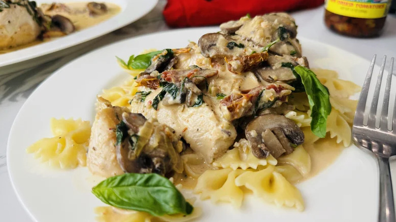 Classic creamy Tuscan chicken served on a bed of pasta on a white plate with a fork on the side.