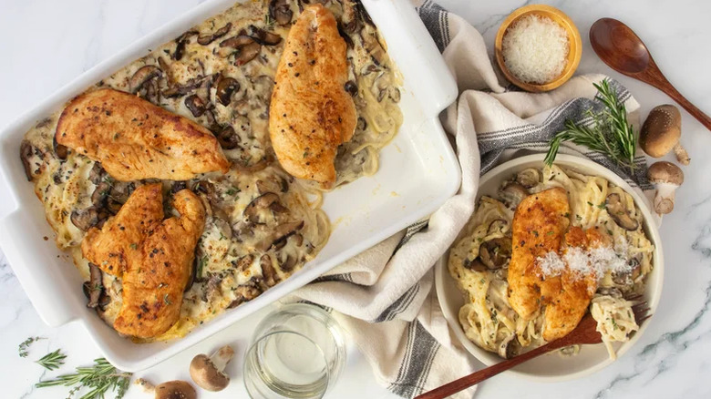 Elevated chicken tetrazzini served from a large white baking dish with a plated portion on the side, a small bowl of salt, and fresh herbs.
