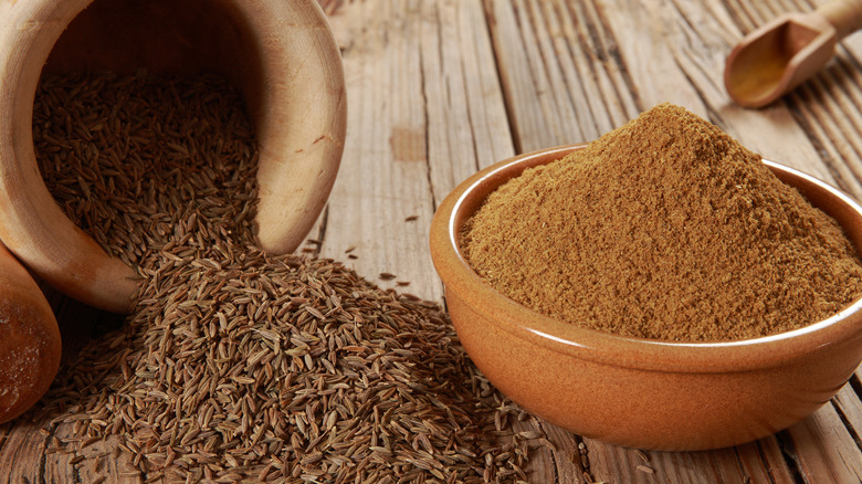 A large bowl full of cumin beside a pile of seeds.