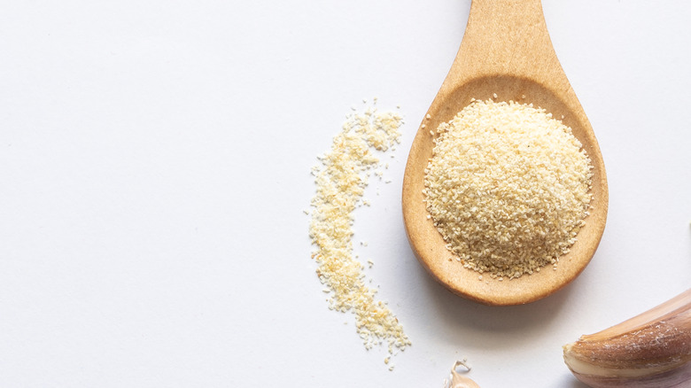 A wooden spoonful of garlic powder with a garlic clove in the frame.