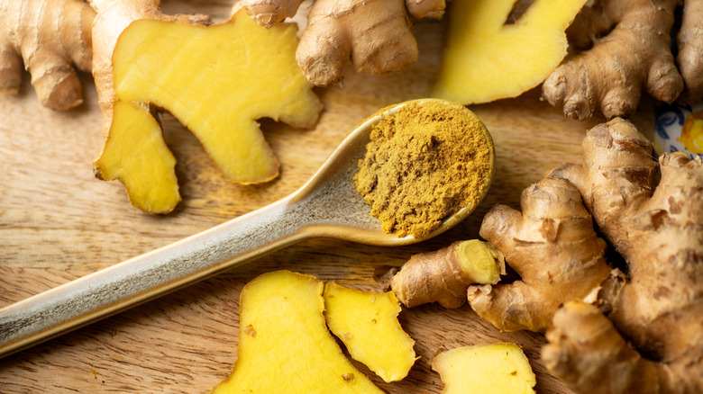 A wooden spoon full of ground ginger is surrounded by fresh ginger