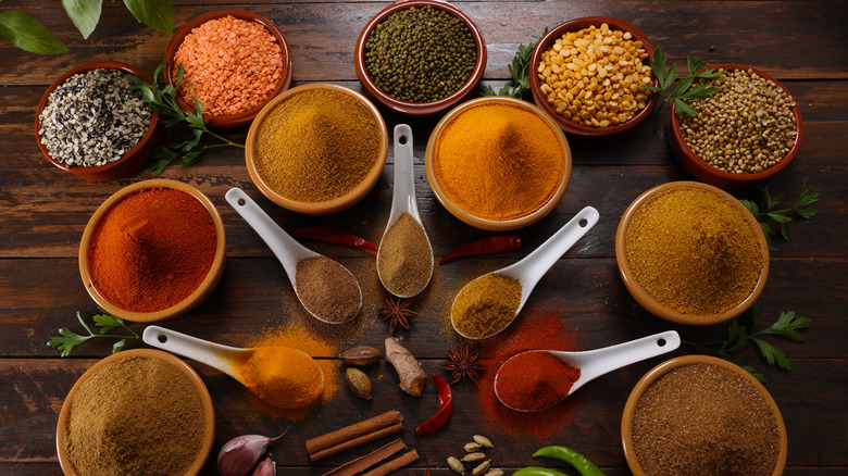 A wide variety of seasonings in bowls and spoons are photographed from above.