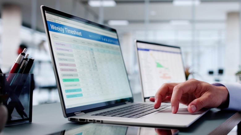 Someone's hand on the keyboard of a laptop displaying timesheet information