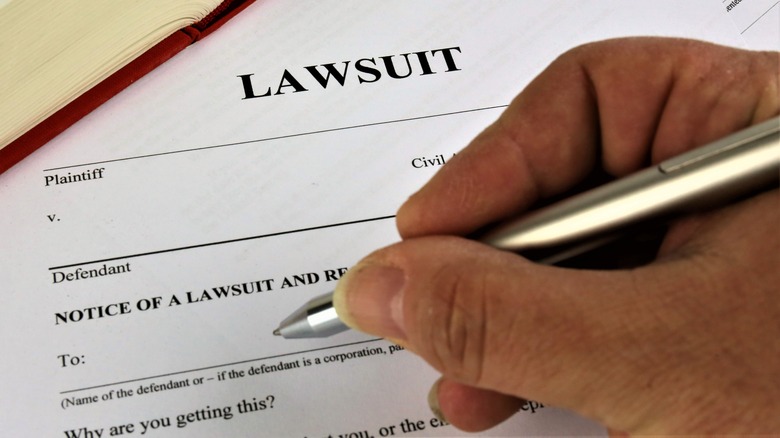 A hand holding a pen over a form with the word "Lawsuit" at the top