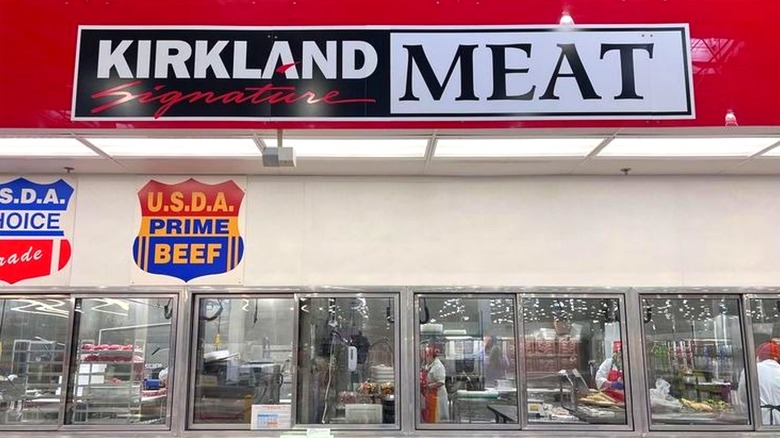View of meat department inside Costco with employees prepping foods behind glass