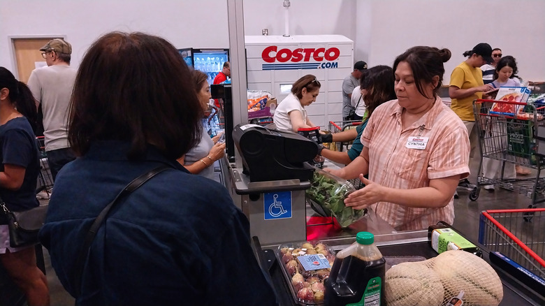 A woman at the Costco checkout buys salad, eggs, and melon