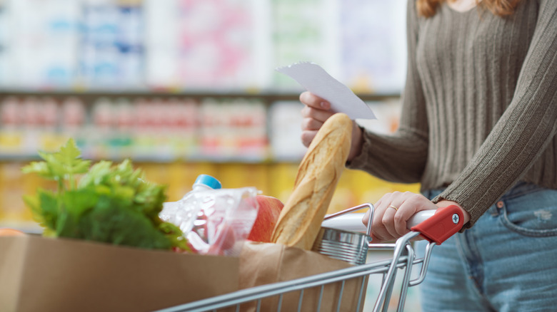 Woman looking at shopping list while holding grocery cart