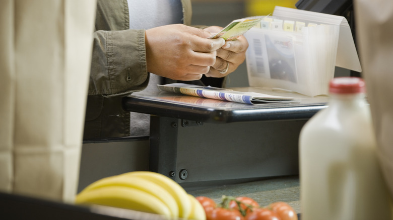 Woman using coupons at grocery store cashier till