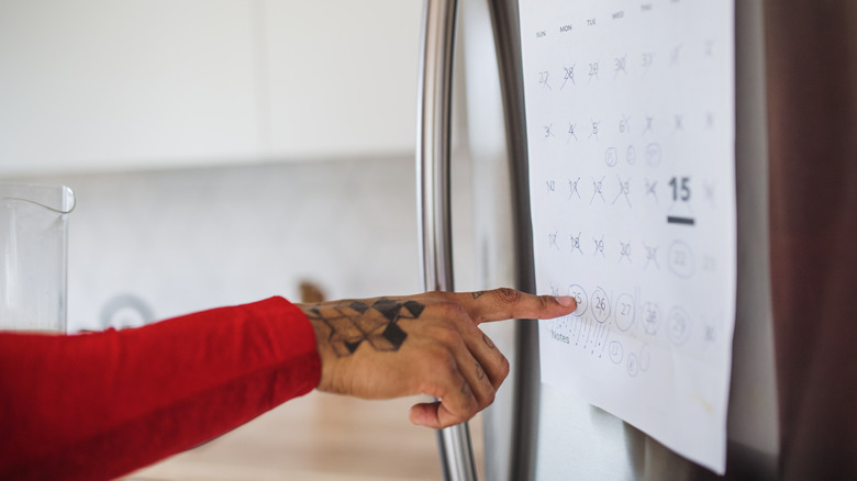 Hand pointing to circled dates on calendar in kitchen