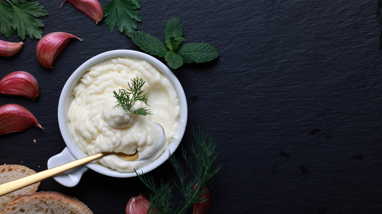 A bowl of aioli with dill and garlic cloves