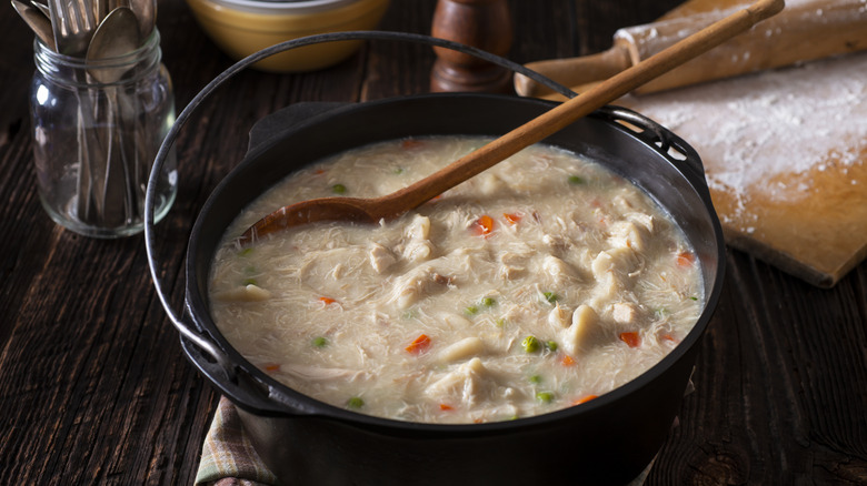 Chicken and dumplings are shown in a pot on a wooden table.