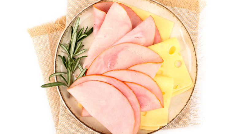 A plate has ham and Swiss cheese slices with a sprig of rosemary.