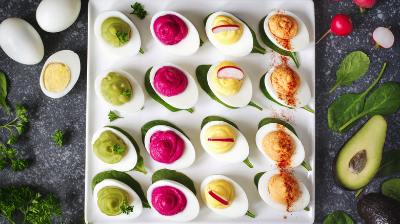 A white square plate with different styles of deviled eggs