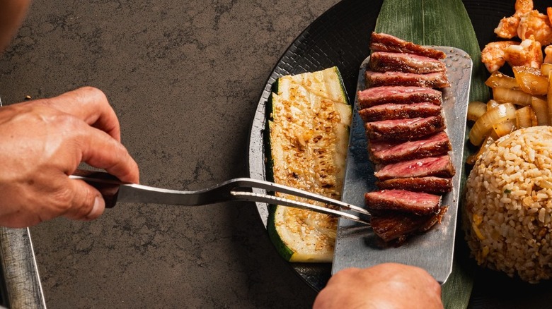 A chef adding steak to a plate with rice and vegetables at Benihana