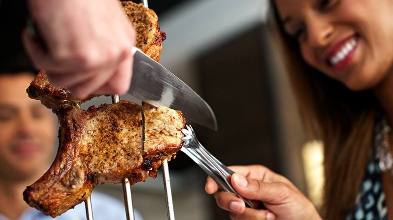 A person carving a piece of meat tableside at Fogo de Chão