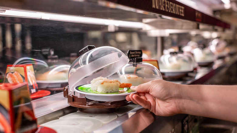 A person taking a plate of sushi off a conveyor belt at Kura Revolving Sushi Bar