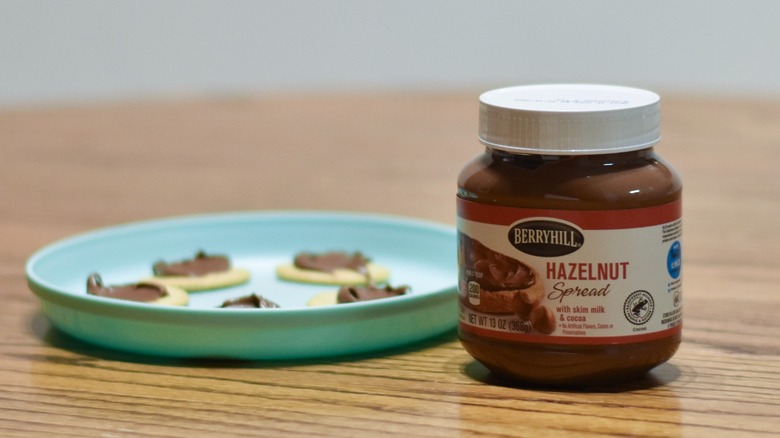 A jar of hazelnut spread next to a plate of crackers with spread on them