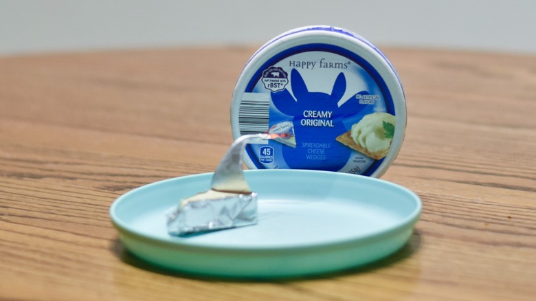 A container of Happy Farms spreadable cheese next to an opened wedge on a plate