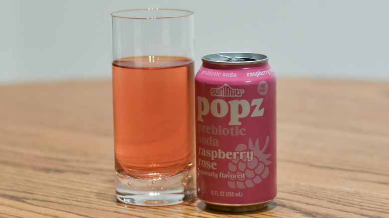 A can of Popz next to a glass of soda on a wooden table